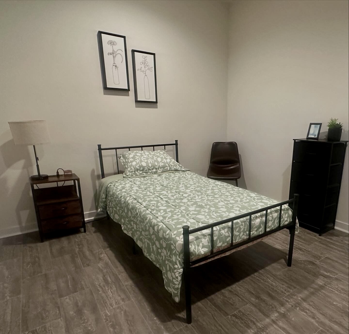 Resident bedroom with green floral bedding, nightstand and dresser